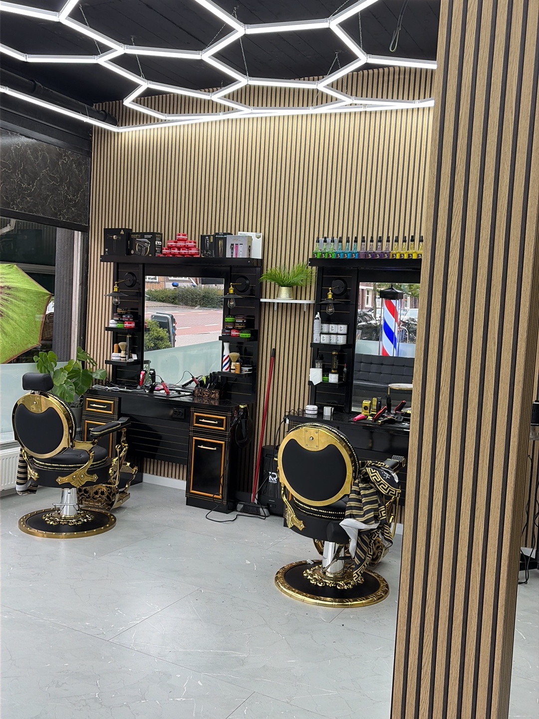 Twee zwart-gouden kappersstoelen voor de spiegelkasten, onder het zeshoekige LED-plafond