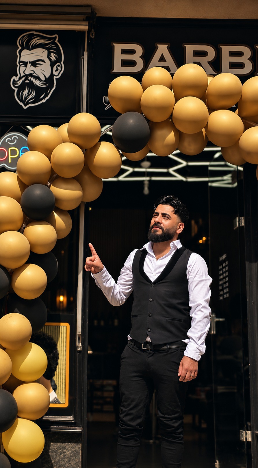 Barbier in zwart gilet bij de ingang van de zaak, onder een boog van gouden en zwarte ballonnen