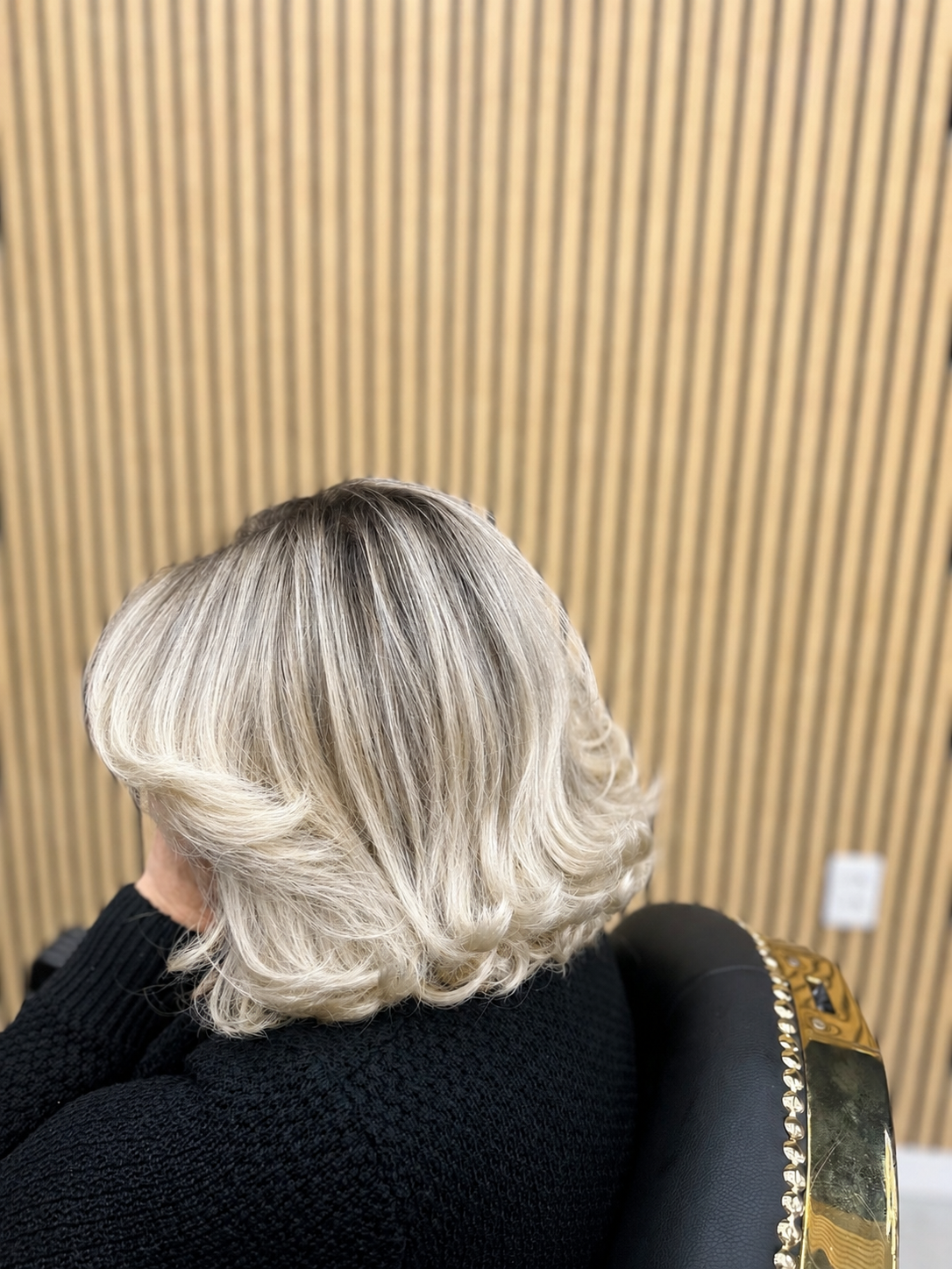 Blond, gelaagd kapsel van achteren, mooi in model geföhnd, voor een wand van houten lamellen